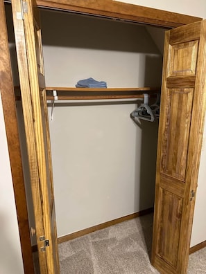 A closet with a wooden door, a hanging rod, and a folded item on top. - Cozy Killington Mountain Retreat with Hot Tub (Killington)