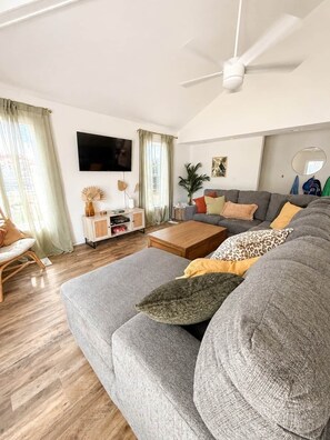 A modern living room with a grey sofa, a wooden coffee table, and a ceiling fan. - Palmetto Safari Retreat (Horry County)
