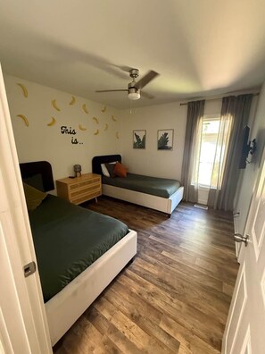 A bedroom with two beds, a ceiling fan, a dresser, and a window with curtains. - Palmetto Safari Retreat (Horry County)