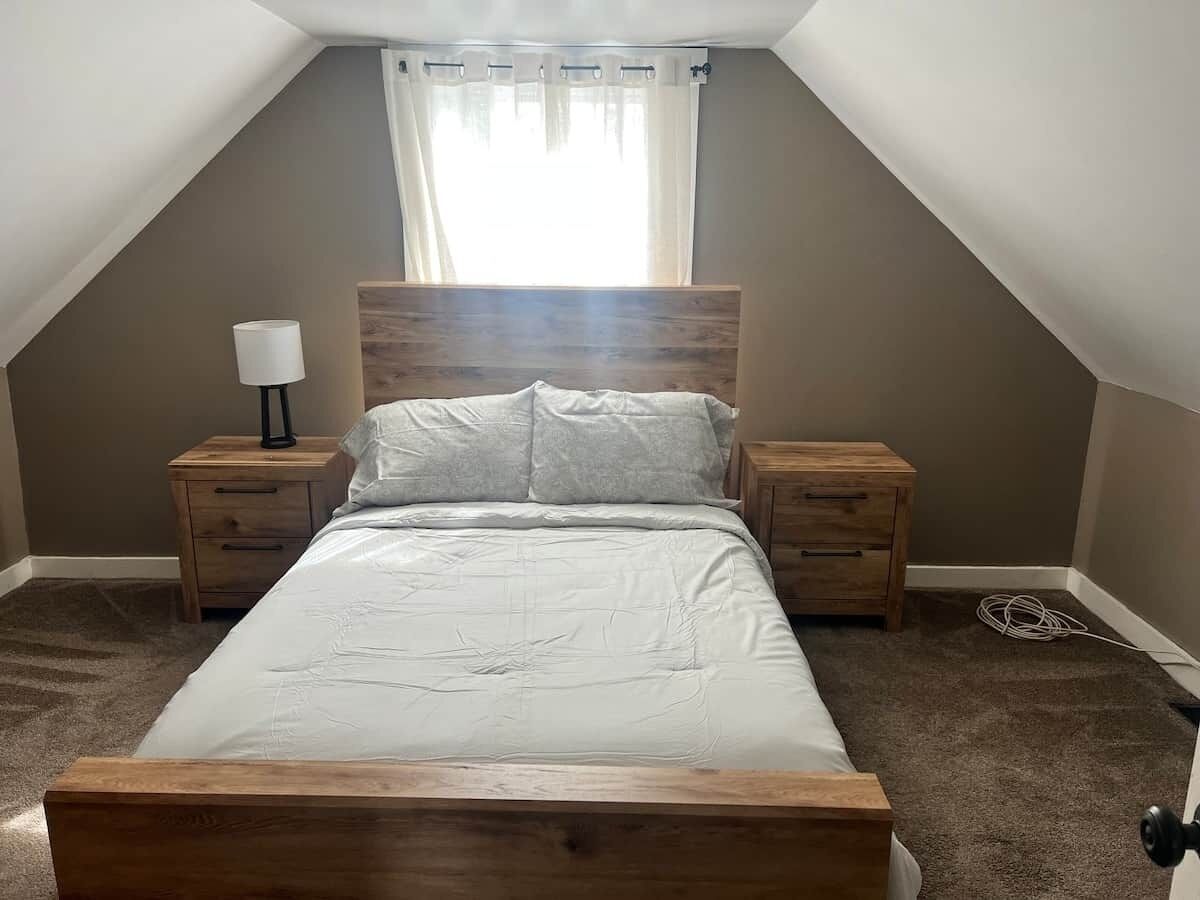 Une chambre à coucher avec un lit en bois, deux tables de chevet, une lampe et une fenêtre avec des rideaux.
