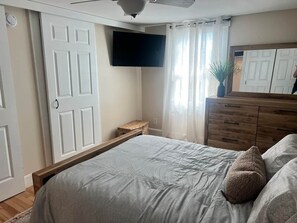 Une chambre à coucher comprenant un lit, un téléviseur à écran plat, une commode et une fenêtre avec des rideaux.