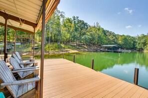 Eine Holzterrasse mit Stühlen, die auf einen ruhigen See mit Bäumen im Hintergrund blickt.