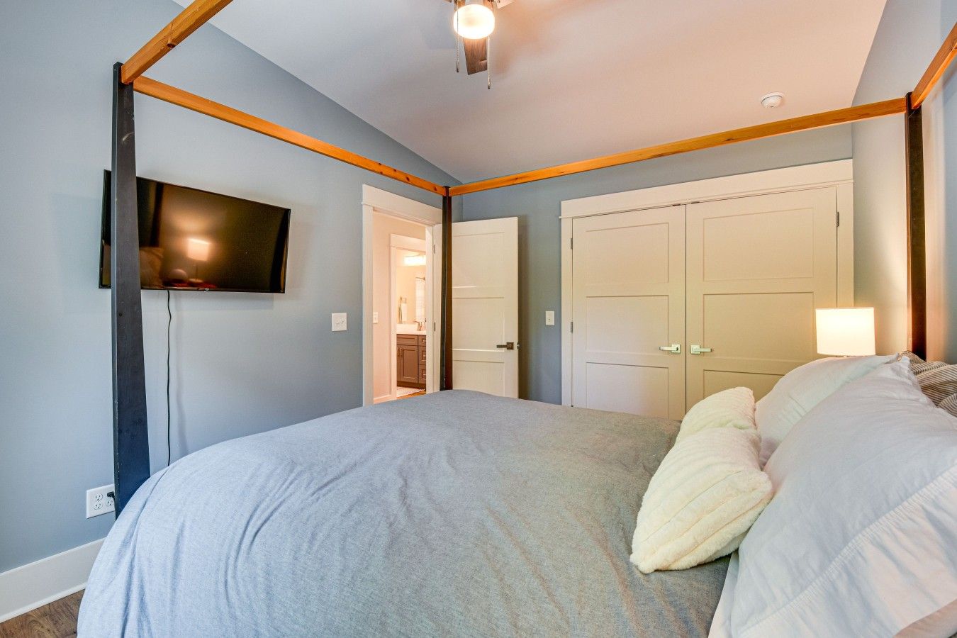 A bedroom with a bed, a television mounted on the wall, and a door leading to a bathroom.