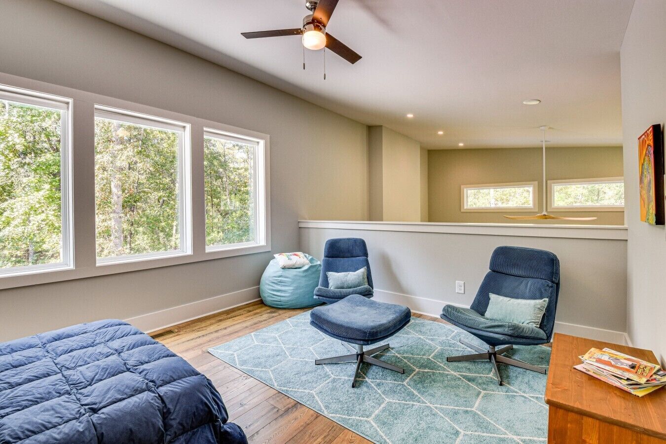 A room with a bed, two chairs, a bean bag, and a table with magazines.