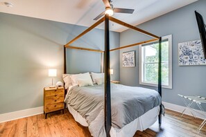 Ein Bett mit Baldachin und Holzrahmen, ein Nachttisch mit Schubladen, eine Lampe und ein Fenster mit Blick auf Grünflächen.