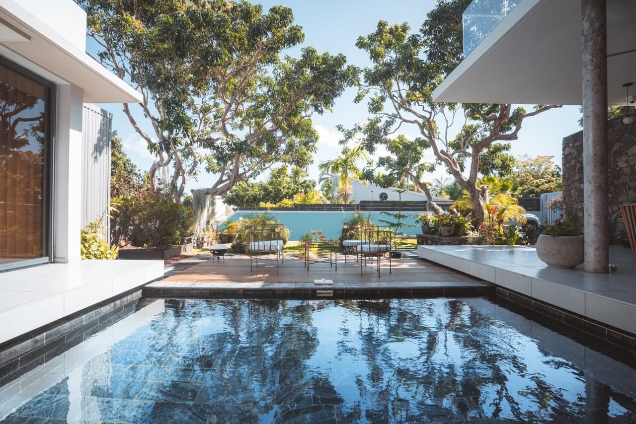 A modern outdoor pool area with a clear view of the sky, surrounded by trees and a stone wall.