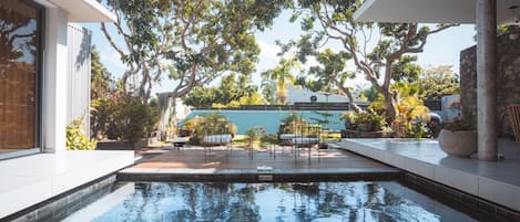 A modern outdoor pool area with a clear view of the sky, surrounded by trees and a stone wall.