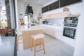 A modern kitchen with a central island, bar stools, a built-in oven, and a stone wall. - Villa Camilla | Private Pool & Serenity | Saint-Pierre • Reunion Island (Saint-Pierre)