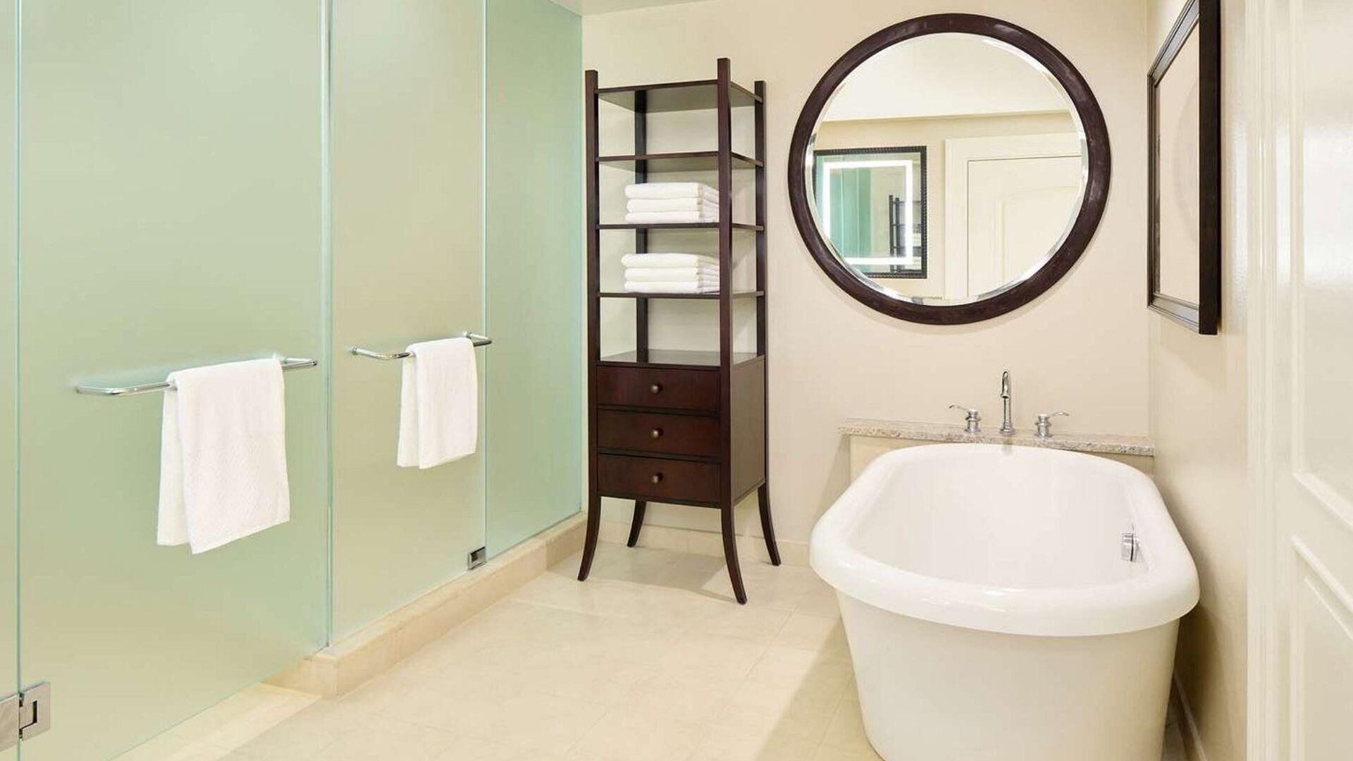 A bathroom with a bathtub, a glass shower enclosure, a wooden towel rack, and a mirror.