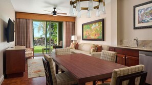 A spacious living area with a large wooden table, a sofa, and a television mounted on the wall.