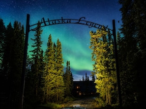 A wooden sign with 'Alaska Legend' written on it, set against a night sky with visible stars and the Northern Lights. - Alaska Legends Kenai River Lodge (Soldotna)