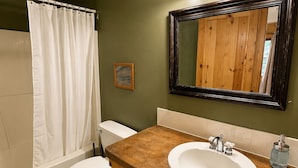 Une salle de bain avec un meuble-lavabo en bois, un lavabo blanc, un miroir et un rideau de douche.