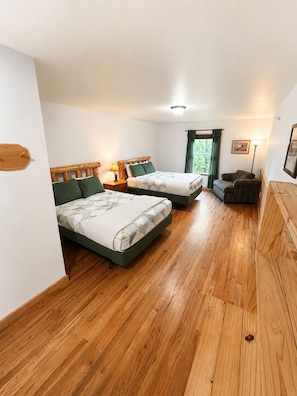 A room with two beds, a wooden floor, a window with curtains, and a chair. - Alaska Legends Kenai River Lodge (Soldotna)
