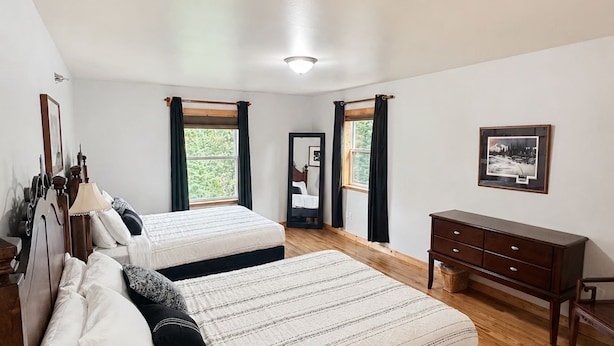 Une chambre avec deux lits, un plancher en bois, une commode et un tableau encadré au mur.