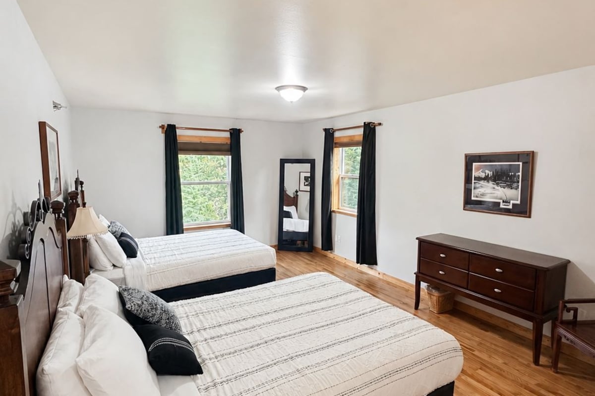 Une chambre avec deux lits, un plancher en bois, une commode et un tableau encadré au mur.