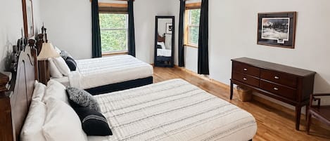 A bedroom with two beds, wooden flooring, a dresser, and a framed picture on the wall.