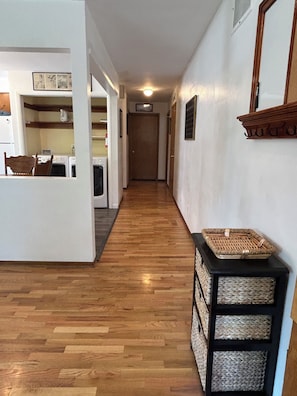 A hallway with wooden flooring, a black console table with baskets, and a door at the end. - Bright & Cozy 2 BR 1 BA house, fenced & pet friendly, garage & driveway parking. (Yakima)