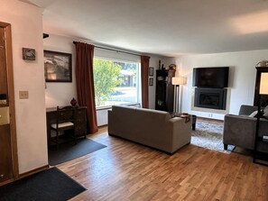 Un salon avec un canapé, une cheminée, un téléviseur et une fenêtre avec des rideaux.