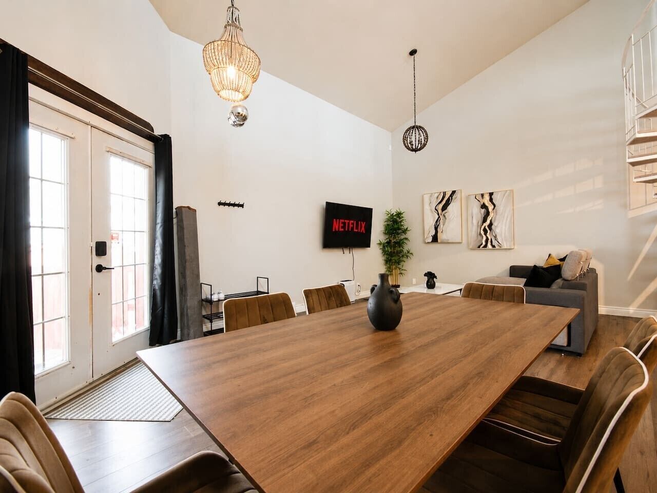 Uma sala de estar moderna com uma grande mesa de jantar de madeira, um sofá e uma TV fixada na parede.