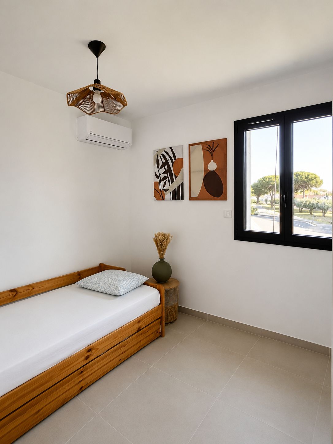 Ein schlichter Schlafzimmerraum mit einem hölzernen Bett, einer Pendelleuchte und zwei an der Wand befestigten Kunstwerken.