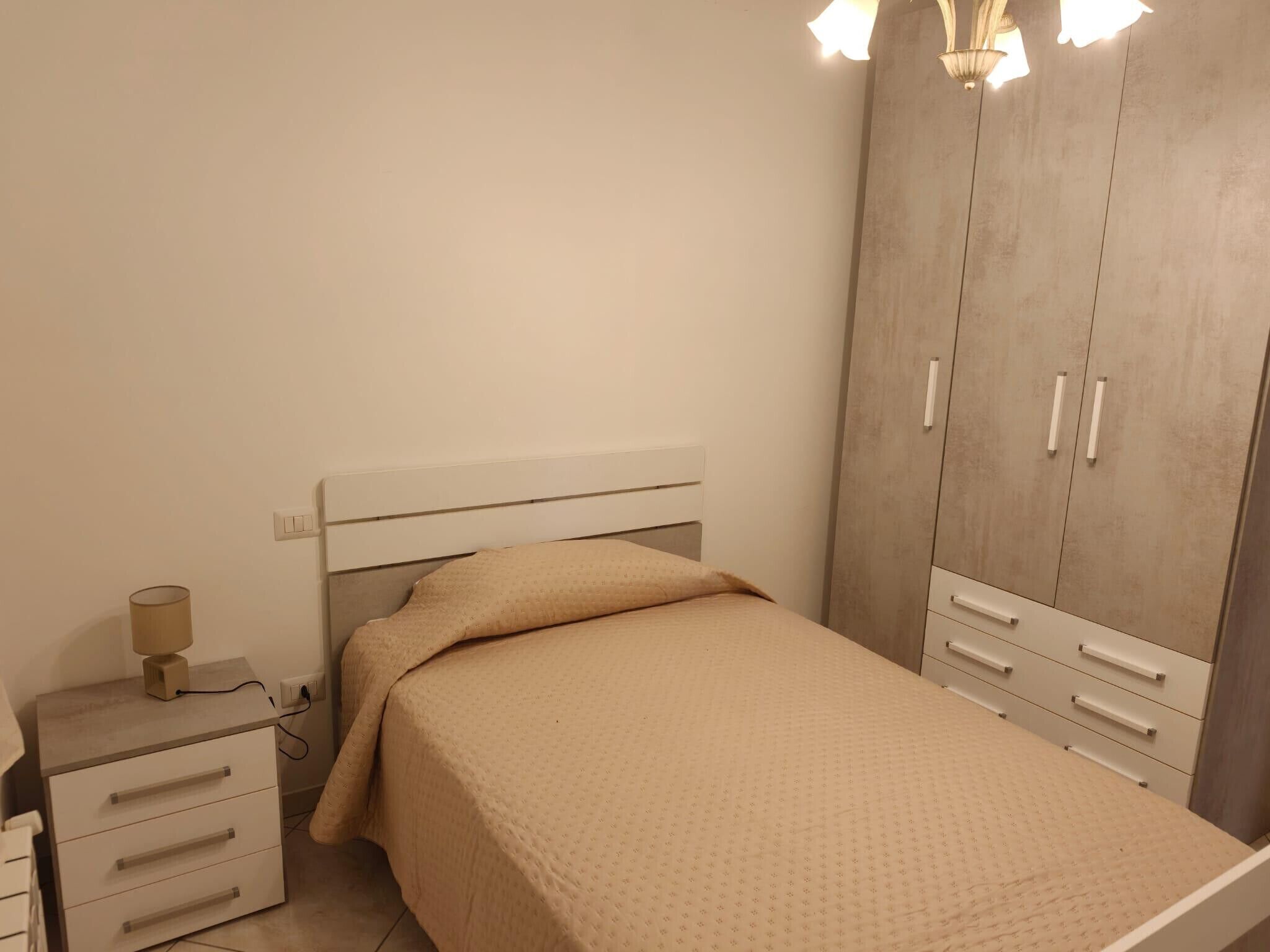 A bedroom with a bed, bedside table, lamp, and wardrobe.