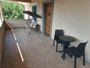 Ein Balkon mit einer Schaukelstuhlsitzgruppe, einem Tisch und zwei Stühlen sowie einer Tür.