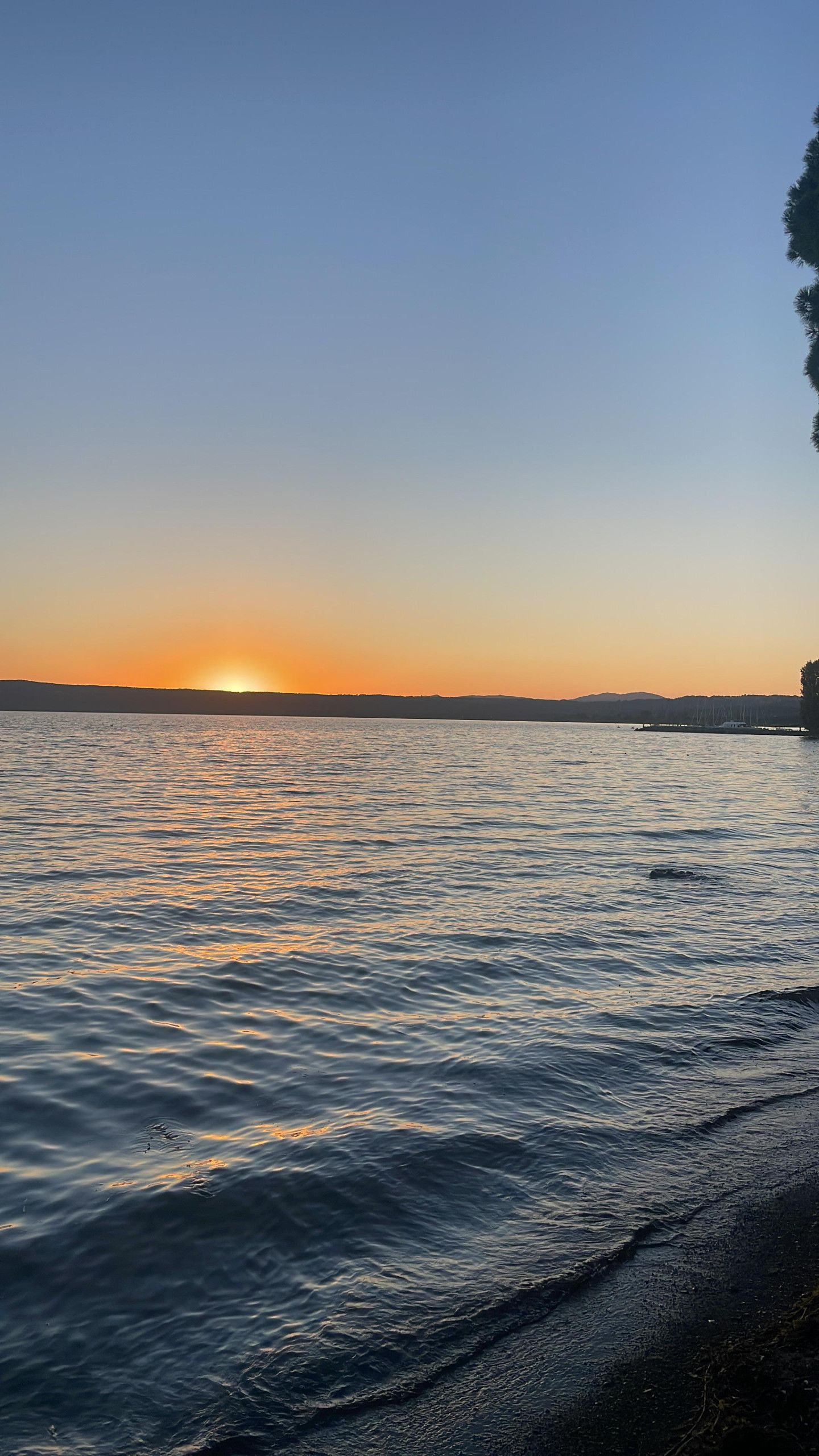 A sunset over a calm body of water with a distant shoreline.