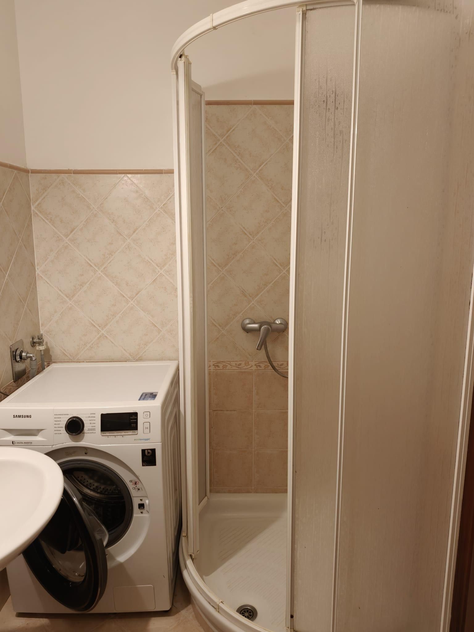 A bathroom with a washing machine, a shower, and a sink.