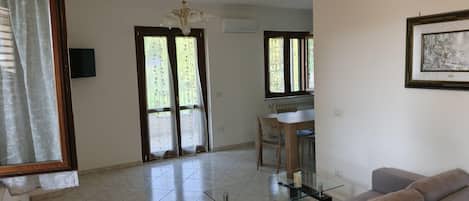 A spacious living area with a glass coffee table, a sofa, a dining table with chairs, and a chandelier.