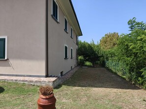 Ein Gebäude mit einem Steinweg, der zu einer Rasenfläche führt, umgeben von Bäumen und einem Zaun.
