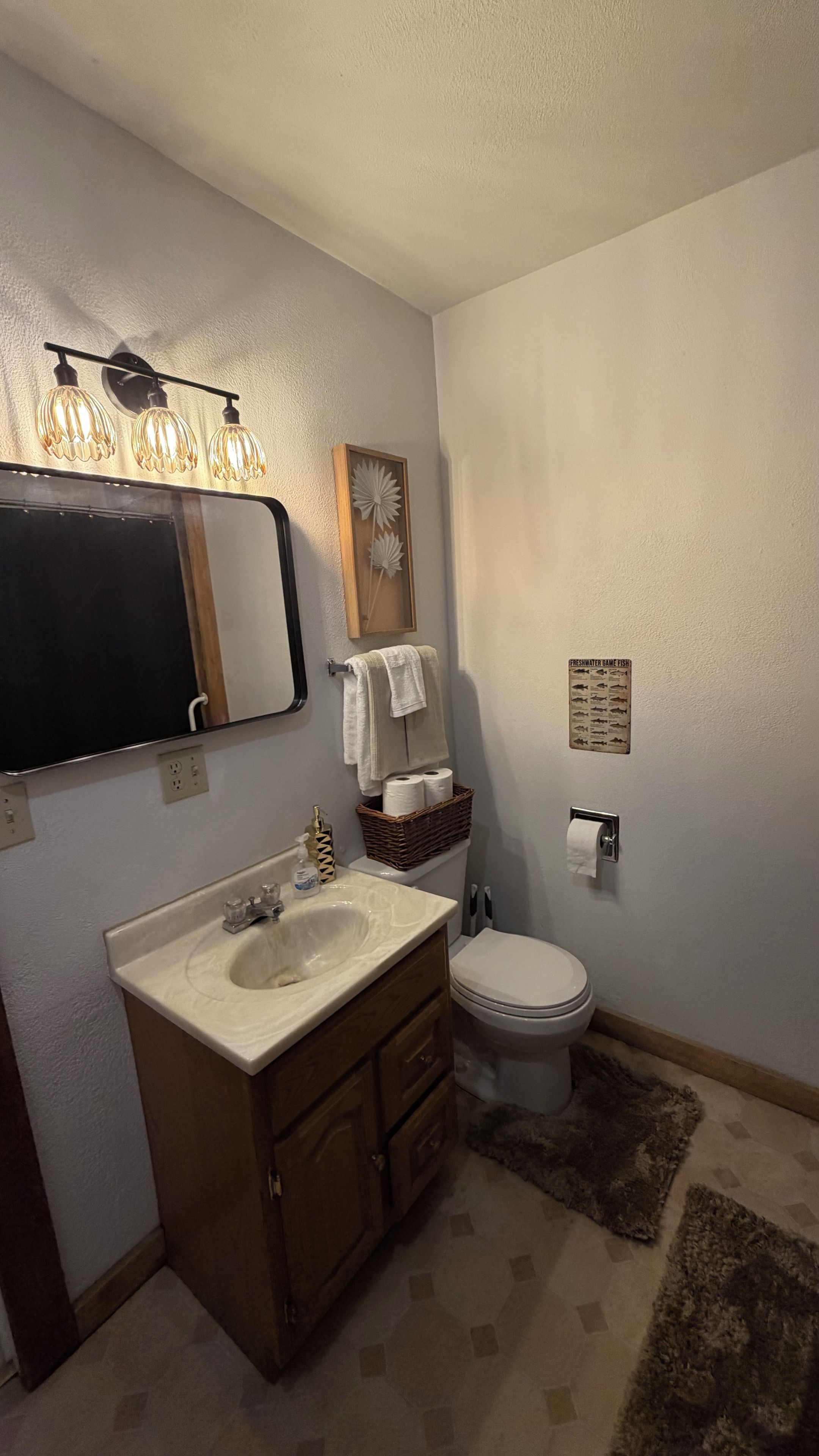 A bathroom with a sink, mirror, towel rack, toilet, and a decorative wall piece.
