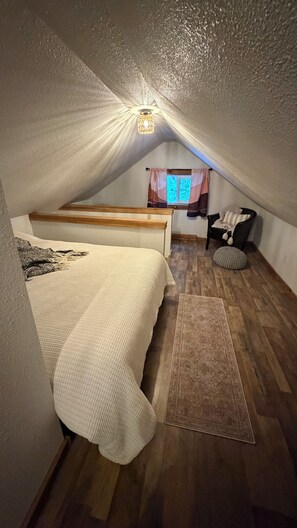 Ein gemütliches Schlafzimmer im Dachgeschoss mit einem Bett, einem Sessel und einem Fenster.