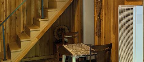 A wooden interior with a staircase, a dining table with chairs, a patterned rug, and a white appliance.