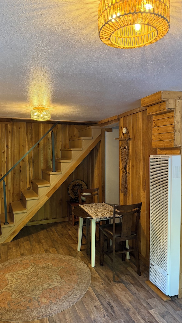 Un intérieur en bois avec un escalier, une table à manger avec des chaises, un tapis à motifs et un appareil électroménager blanc.