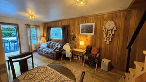 A cozy room with a wooden floor, a sofa, a chair, a small table, and a dreamcatcher on the wall.