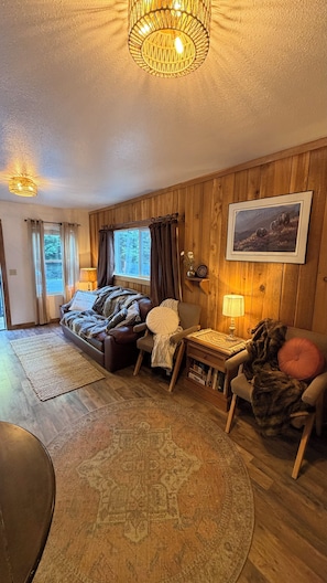 A cozy living room with a wooden floor, a sofa, a chair, a table, and a lamp.