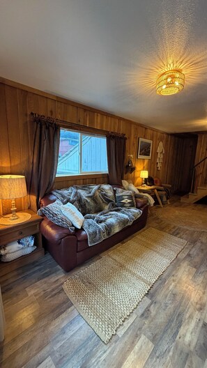 Un salon chaleureux avec un canapé en cuir, une grande fenêtre avec des rideaux, un lustre et un plancher en bois.