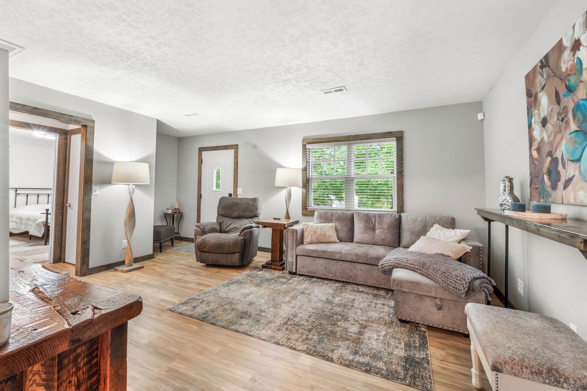 A spacious living room with a sofa, armchairs, a coffee table, and a large window with blinds.