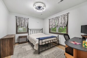 Une chambre à coucher comprenant un lit, un bureau, une chaise, un téléviseur et une fenêtre avec des rideaux.
