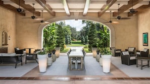 Un patio interior con vistas a un jardín ajardinado, que incluye una mesa y sillas de comedor, plantas en macetas y un techo con vigas a la vista.
