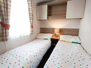 A bedroom with two single beds, a bedside table with a lamp, and a built-in shelf above the beds. - Cala Gran Holiday Park - Holiday Accommodation 20111 (Fleetwood)