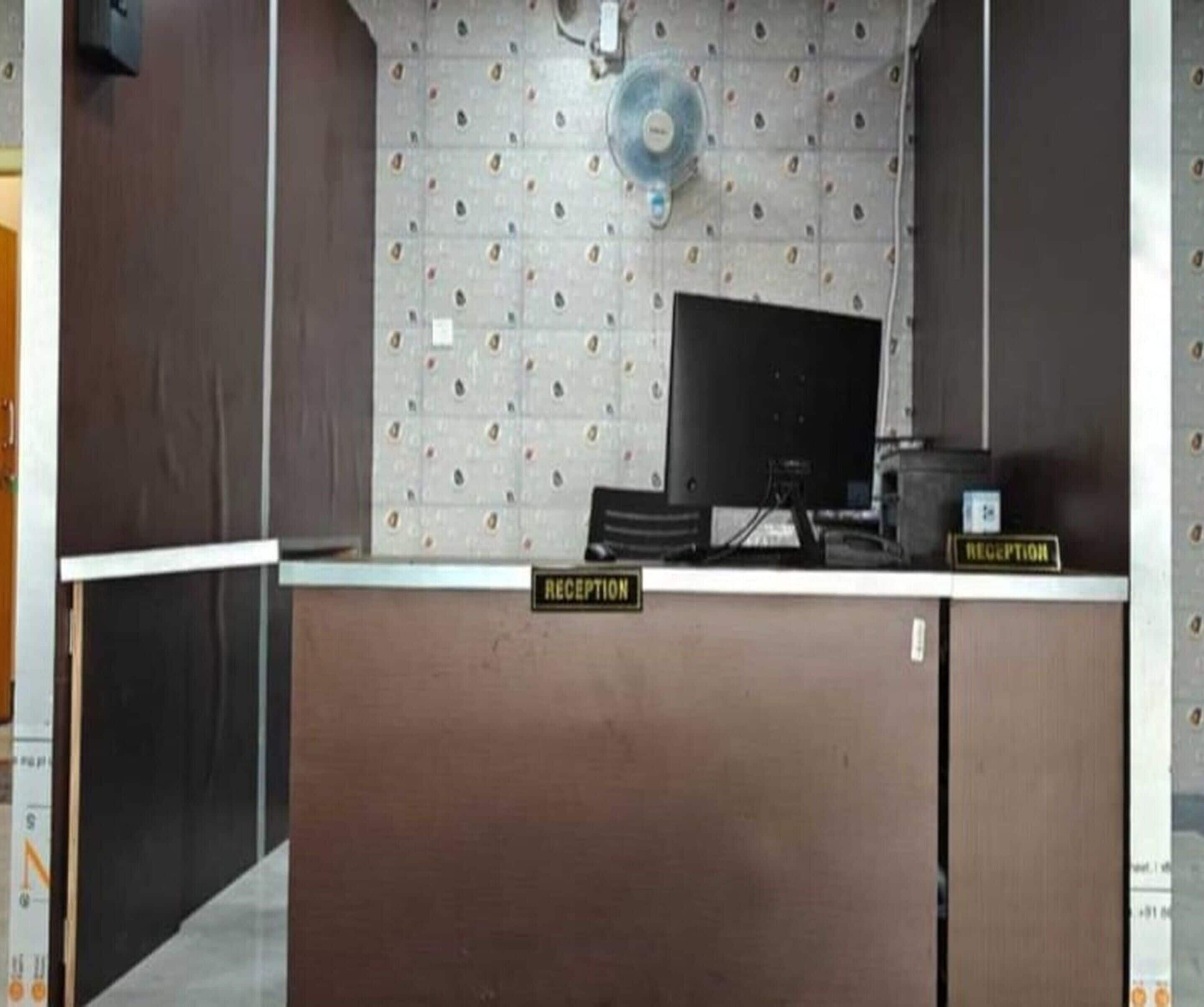 Una reception con una insegna che riporta la scritta 'RECEPTION', un monitor per computer e una ventola a parete.