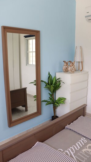A bedroom with a large mirror, a dresser, a potted plant, and striped bedding. - CasaMIA RD: Your Caribbean Getaway. (Río San Juan)