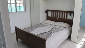 Een slaapkamer met een houten bedframe, een witte matras en streepjesbeddengoed.