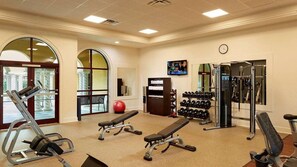 Ein Fitnessstudio mit Kraftgeräten, Bänken, einem roten Trainingsball und einem an der Wand montierten Fernseher.