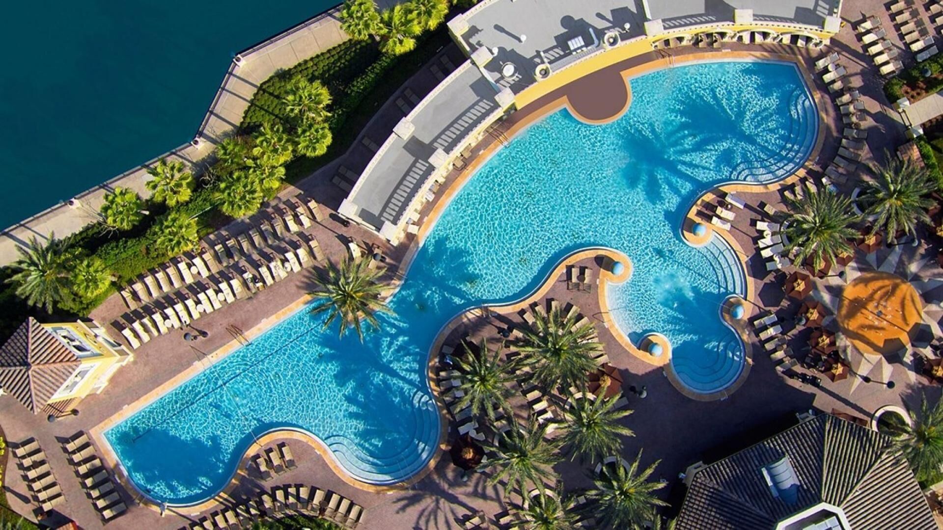 An aerial view of a hotel with a large, winding pool surrounded by lounge chairs and palm trees.