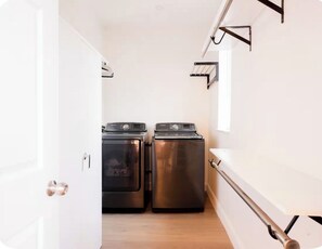 A laundry room with two stainless steel washers and dryers, a white door, and a window on the right. - King Bed Primary • Spacious Boutique Stay (Homestead)