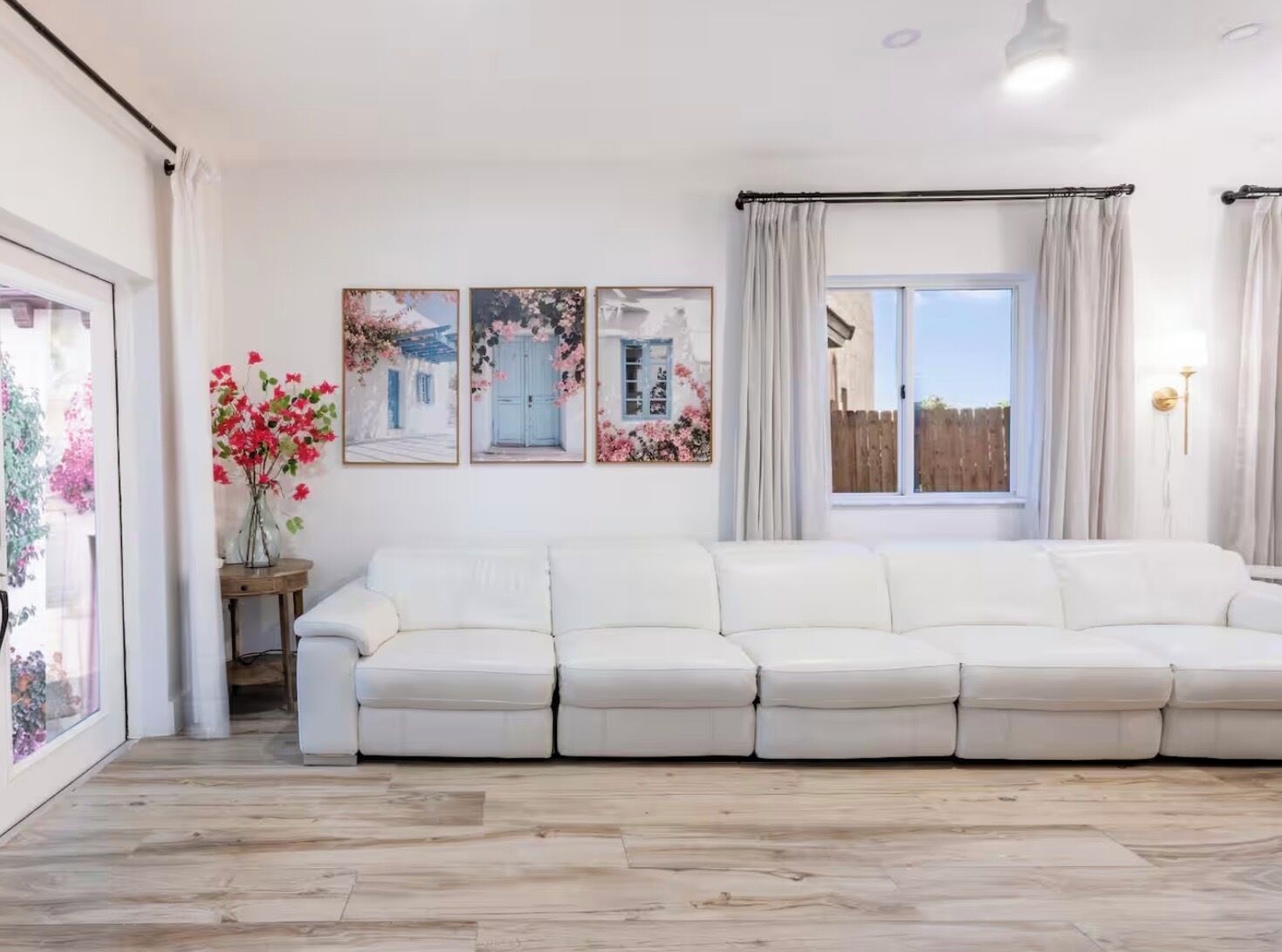 A spacious living room with a white sofa, a wooden floor, and a large window with curtains.