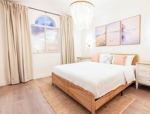 A bedroom with a wooden bed, a large window with curtains, a chandelier, and wall art.