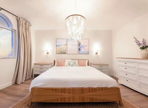 Quarto com cama grande, mesas de cabeceira, cômoda e luminárias fixadas na parede.
